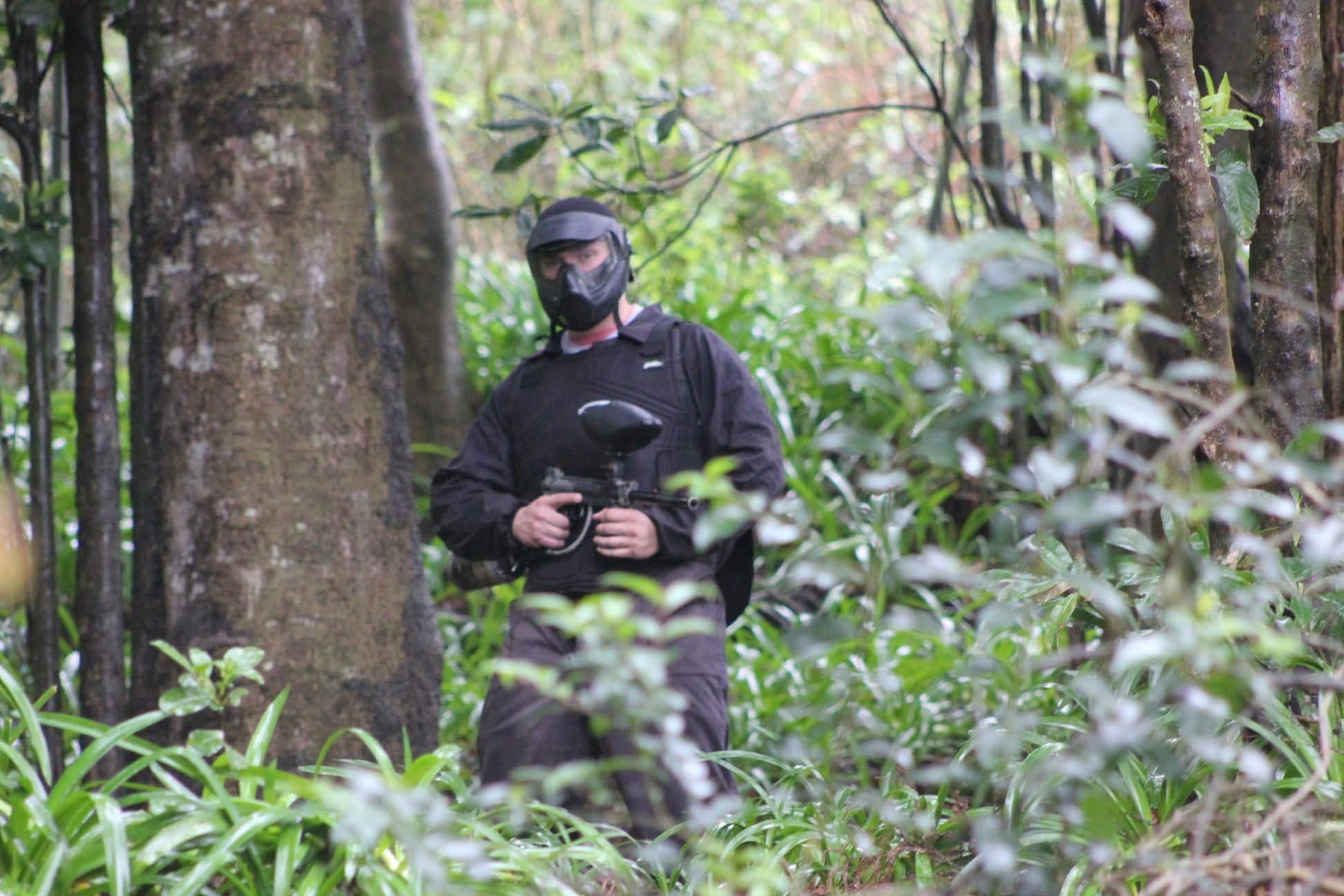 Jogador de paintball equipado a avançar entre árvores