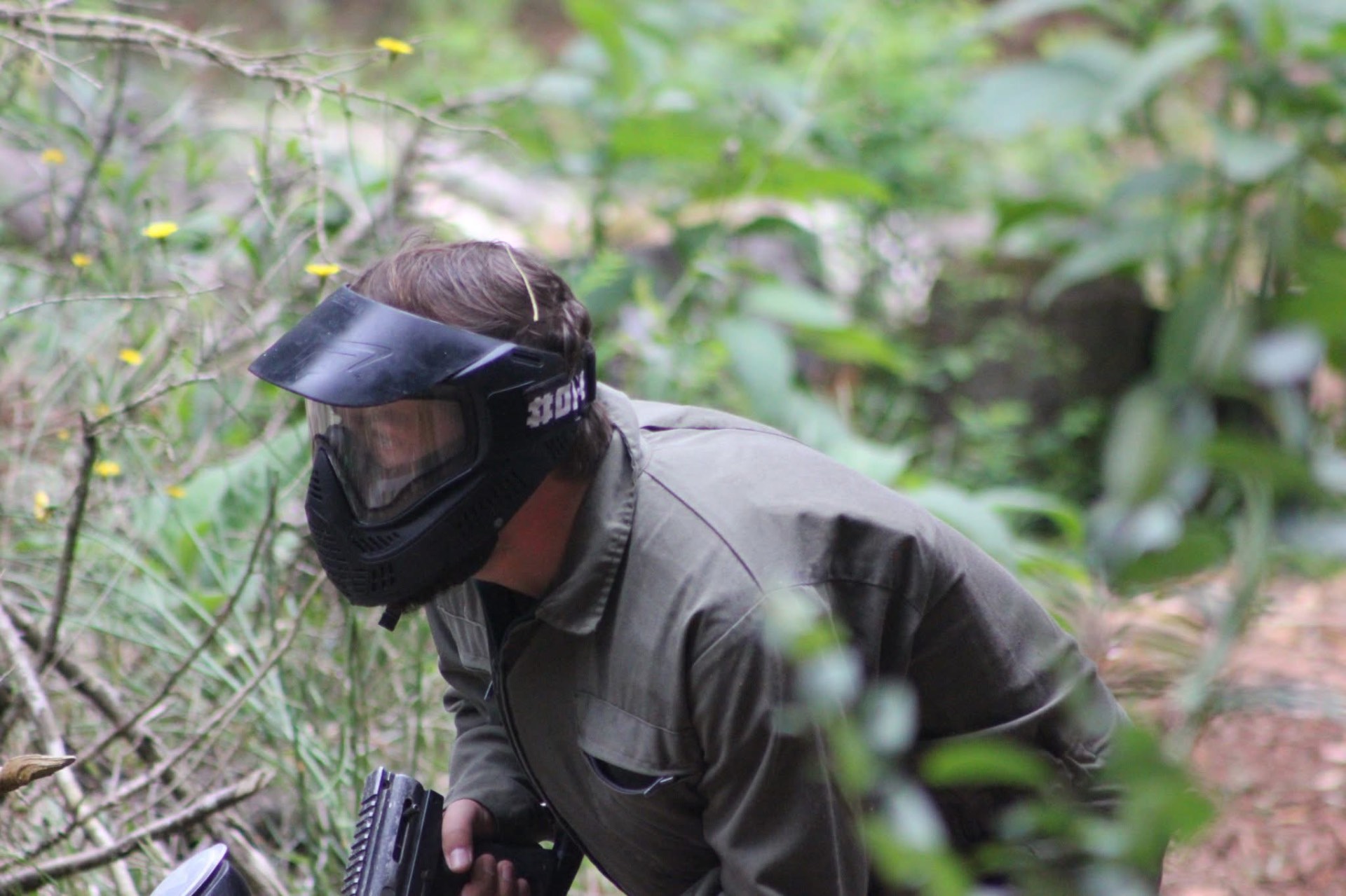Jogador de paintball agachado a avançar pela vegetação